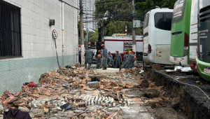 Calçada destruída com concreto quebrado e entulho ao lado de ônibus verdes e brancos estacionados. Pessoas e caminhão ao fundo em dia nublado. Desabamento de muro no Brás deixa três vítimas - Corpo de Bombeiros
