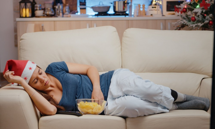 Mulher com sono e chapéu de Papai Noel assistindo televisão no sofá