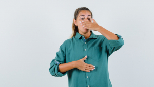 Mulher jovem cobrindo a boca com a mão na blusa verde e parecendo exausta