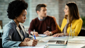 Gerente de banco feminino negro usando laptop e escrevendo notas enquanto se encontra com um casal no escritório