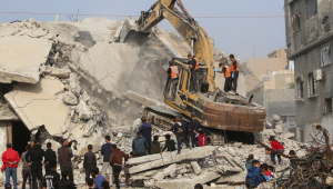 Integrantes da Defesa Civil usam uma escavadeira para procurar os restos de vítimas nos escombros de um prédio destruído no campo de refugiados de Bureij, no centro da Faixa de Gaza