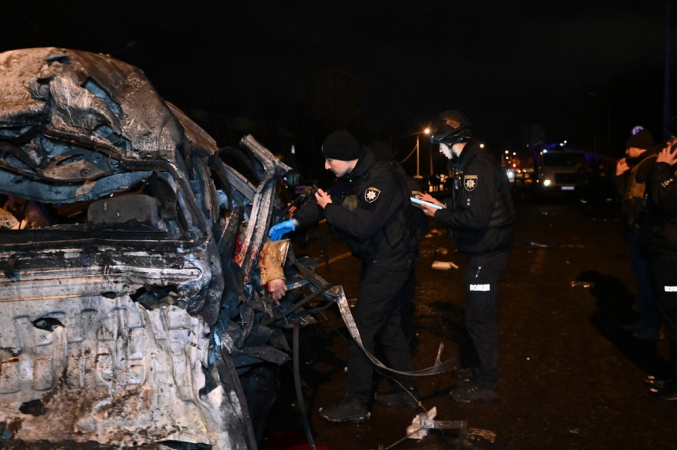 Policiais ucranianos inspecionam um carro destruído com o corpo de uma vítima no local do impacto após um ataque em Kharkiv
