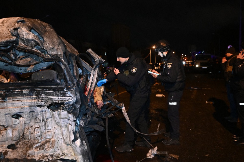 Policiais ucranianos inspecionam um carro destruído com o corpo de uma vítima no local do impacto após um ataque em Kharkiv