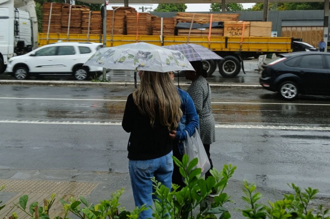 Pedestres se protegem da chuva em ponto de ônibus no bairro de Interlagos, na zona sul de São Paulo