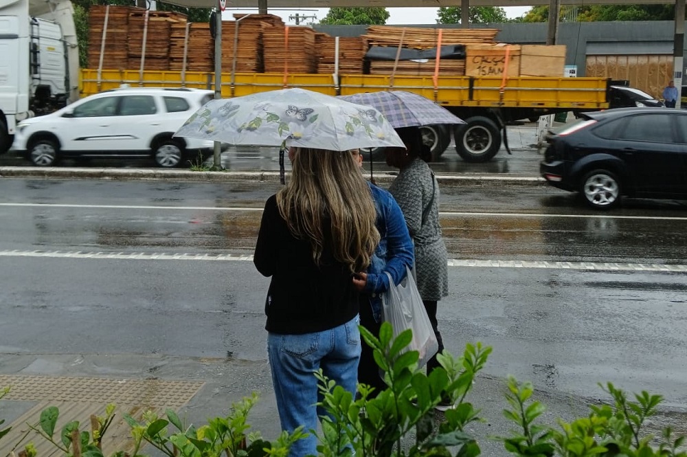 Pedestres se protegem da chuva em ponto de ônibus no bairro de Interlagos, na zona sul de São Paulo