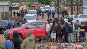 Moradores observam enquanto policiais do Serviço de Polícia Sul-Africano (SAPS) se reúnem no local do ataque a um bar, em Bekkersdal