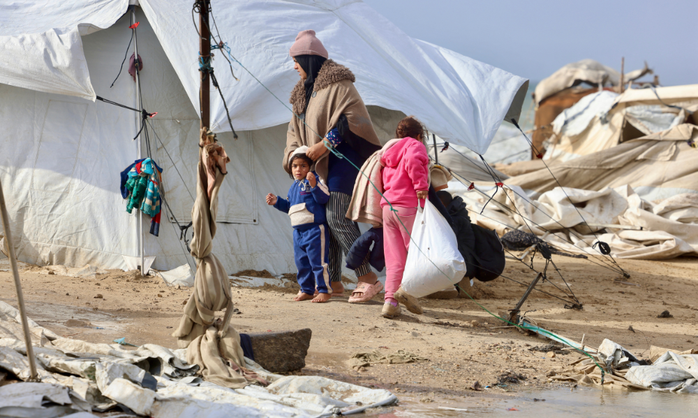 Uma mulher palestina deslocada segura uma criança ao lado de tendas e abrigos improvisados, enquanto a região enfrenta condições climáticas frias de inverno no campo de refugiados de Al-Mawasi, no sul da Faixa de Gaza, em 29 de dezembro de 2025. Iniciado em outubro, um frágil cessar-fogo interrompeu até agora dois anos de guerra entre Israel e o Hamas na Faixa de Gaza, apesar de ambos os lados trocarem acusações de violações da trégua.
