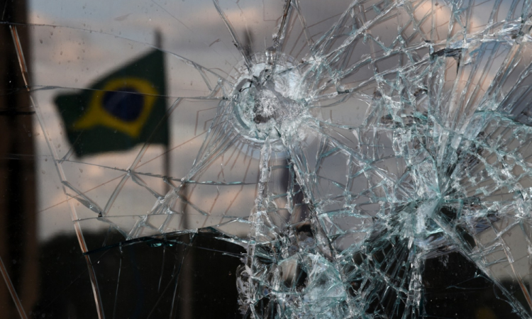 Bandeira brasileira se reflete em uma janela quebrada do prédio do STF em Brasília, dois dias após os ataques de 8 de Janeiro