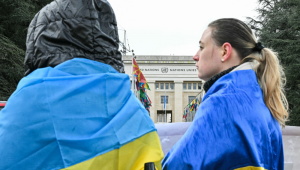 Manifestantes vestindo bandeiras ucranianas se posicionam em frente ao escritório das Nações Unidas enquanto uma nova rodada de negociações entre representantes russos, ucranianos e americanos, com o objetivo de encontrar uma solução para quatro anos de conflito na Ucrânia, ocorre em Genebra em 17 de fevereiro de 2026. (Foto de Harold CUNNINGHAM / AFP)