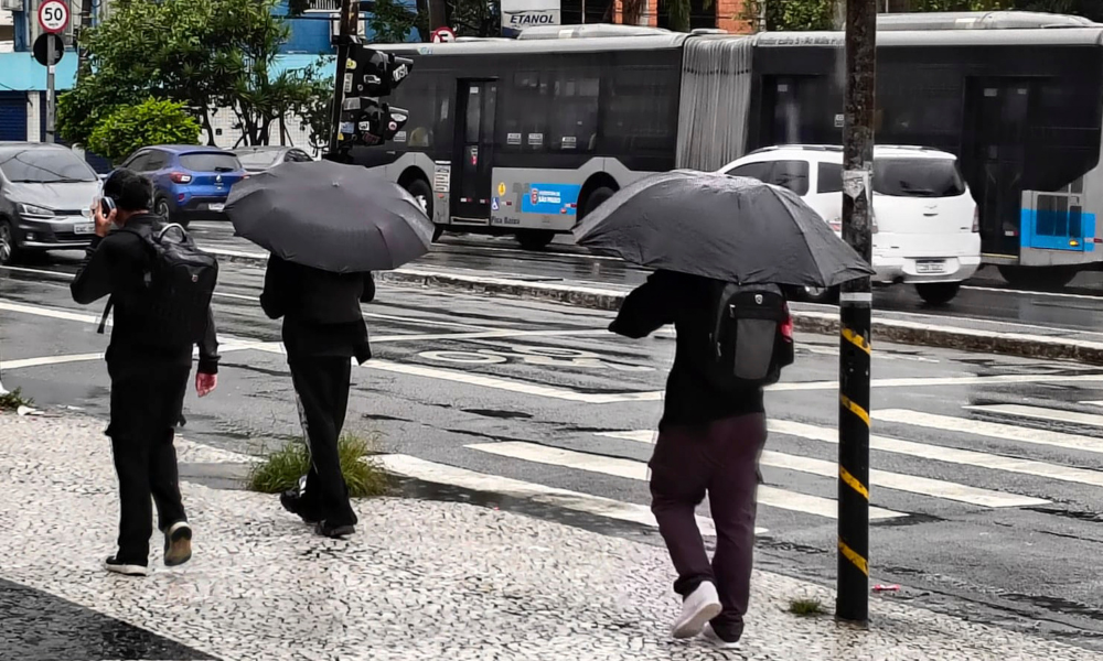 Pedestres se protegem da chuva nas ruas do Jardim Consórcio, na zona sul da cidade de São Paulo, na manhã desta quinta-feira (12)