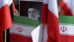 Um manifestante segura um cartaz com a imagem do falecido Líder Supremo iraniano, Aiatolá Ali Khamenei, cercado por bandeiras iranianas, em frente ao consulado dos EUA, durante um protesto contra o conflito no Oriente Médio, na Cidade do México, em 7 de março de 2026. (Foto de Carl de Souza / AFP)