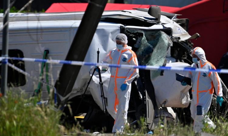 Agentes da Polícia Forense caminham ao lado do ônibus danificado enquanto inspecionam o local do acidente, após um trem colidir com um ônibus escolar, em Buggenhout, na Bélgica