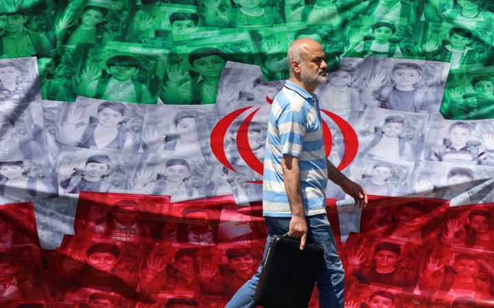 A man walks past an Iranian flag installed along the roadside in Tehran on April 29, 2026, depicting images of children killed on the first day of the war in an alleged US-Israeli missile strike on a school in the southern Iranian city of Minab. US President Donald Trump on April 29 warned Iran to "better get smart soon" as efforts by Washington and Tehran to end hostilities appeared at a standstill.