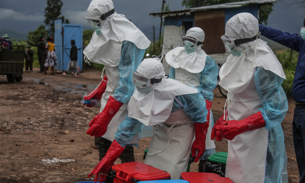 Profissionais de saúde usando equipamentos de proteção individual (EPI) carregam desinfetante no hospital em Rwampara, em 21 de maio de 2026. De acordo com a OMS, o surto mais recente na RDC, o 17º a atingir o vasto país da África Central com mais de 100 milhões de habitantes, já é suspeito de ter causado 139 mortes em quase 600 casos prováveis. Muitos dos casos foram registrados no epicentro da epidemia, na província de Ituri, no nordeste da RDC, muitos em áreas de difícil acesso, assoladas pela série de grupos armados do leste congolês.